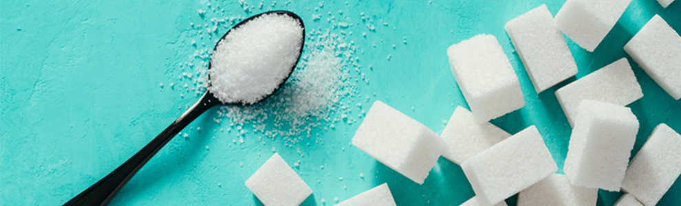 White sugar in a spoon next to numerous sugar cubes